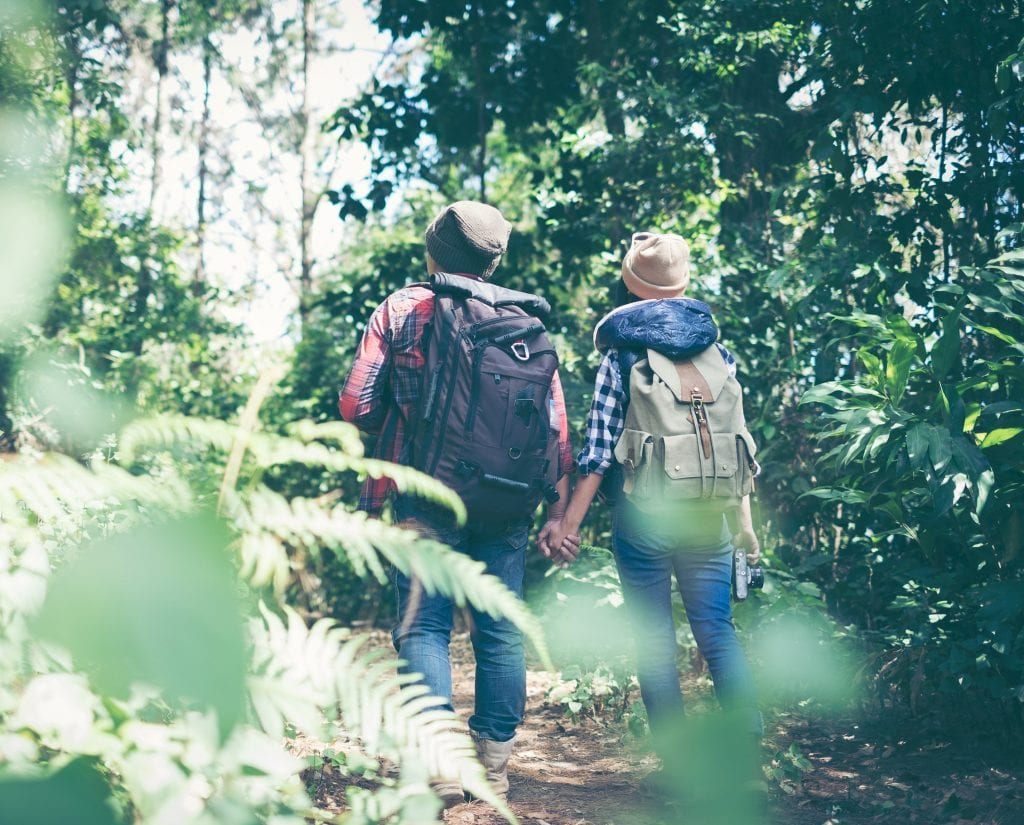 Image of a couple walking in a forest. They are wearing backpacks & stocking hats