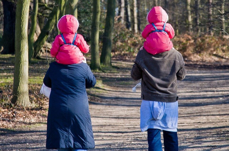 Image of a couple carrying two toddlers in matching pink coats on their shoulders